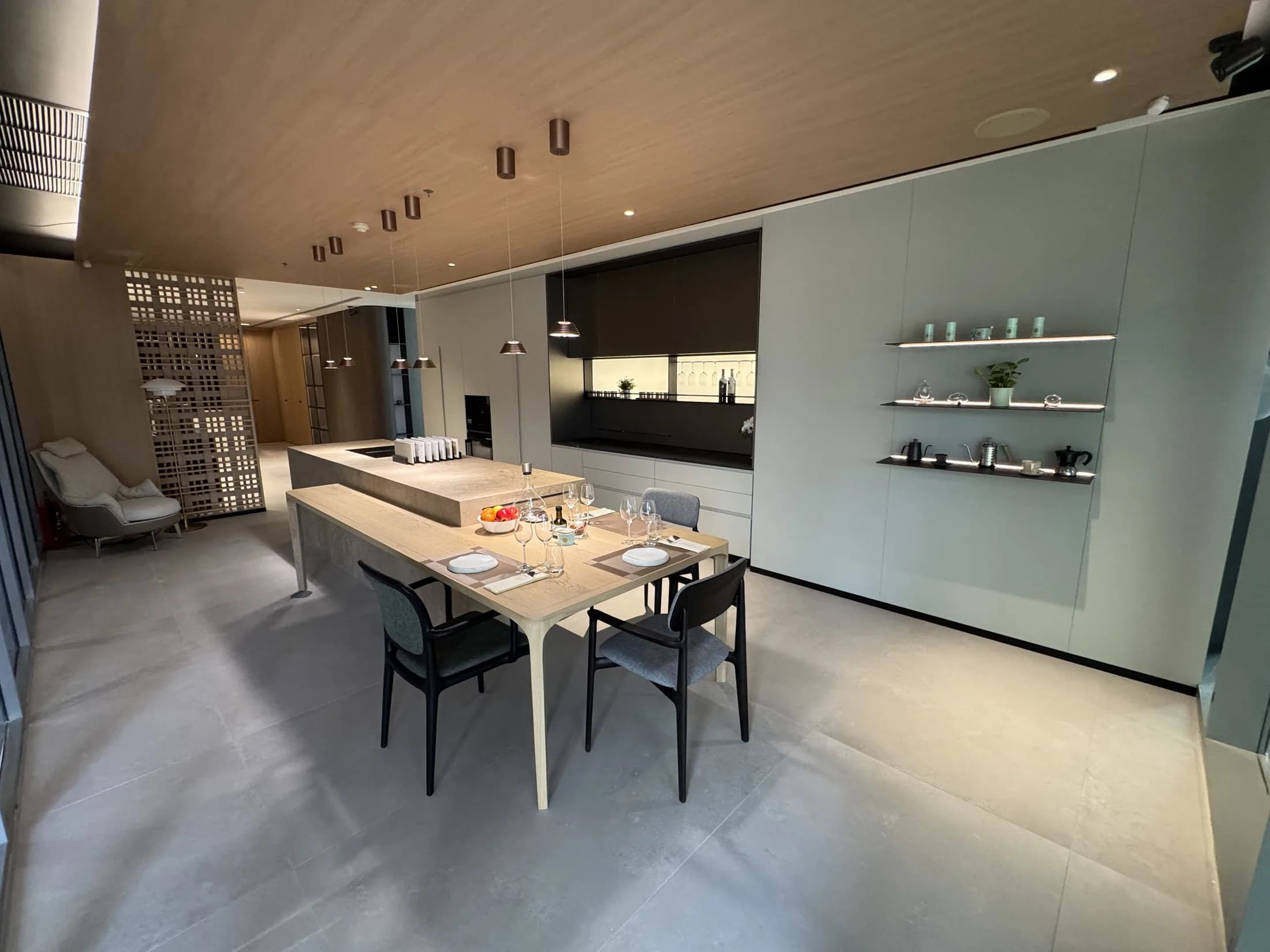 Open-plan kitchen and dining in the Asoke showroom, beneath a warm timber ceiling with a decorative screen